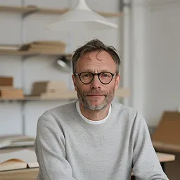 Middle-aged man with glasses and a gray sweater looking at the camera in a home office setting.